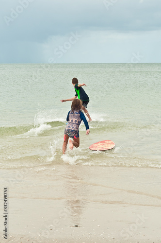 Back view of a young male and female running into tropical waters and getting on a surfboard, in the gulf of mexico on a sunny day