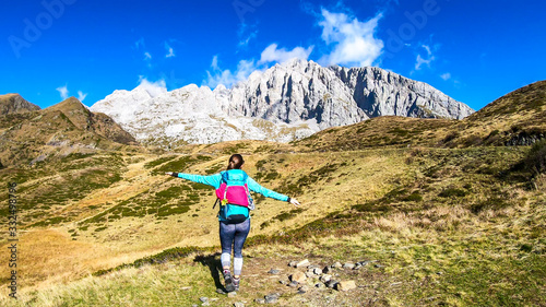 A woman in hiking outfit wandering in Italian Alps. Sharp slopes on both sides of the valley. Hard to reach mountain peaks. There are many mountain ranges in the back. Serenity and calmness. Freshness