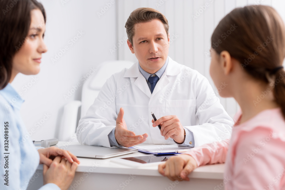 selective focus of ent physician talking to mother and daughter during consultation selective focus of ent physician talking to mother and daughter during consultation