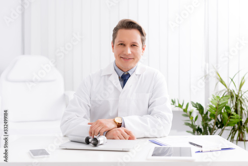 smiling ent physician smiling while sitting at workplace near otoscope photo