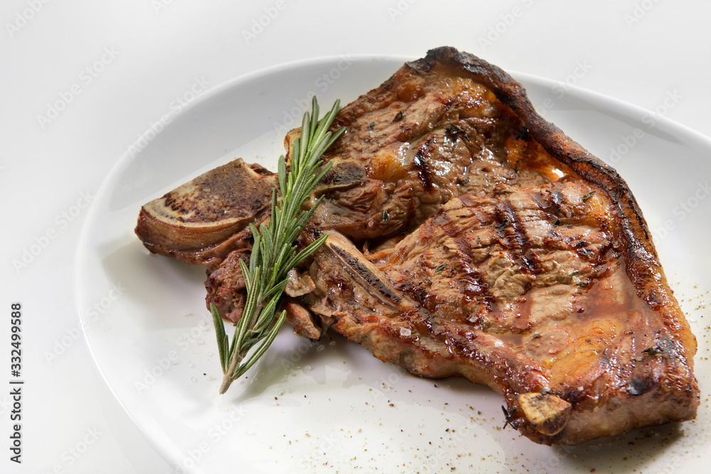 Grilled beef steak with rosemary. Grilled striploin sliced steak. Juicy thick grilled T-bone beef steak seasoned with rosemary fresh of the summer BBQ. Vegetables on a black plate with salt and pepper Grilled beef steak with rosemary. Grilled striploin sliced steak. Juicy thick grilled T-bone beef steak seasoned with rosemary fresh of the summer BBQ. Vegetables on a black plate with salt and pepper