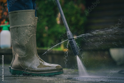Person cleaning a rug or floor mat with the use of a high pressure water cleaner. Cleaning mats with high pressure jet while wearing plastic boots © Anze