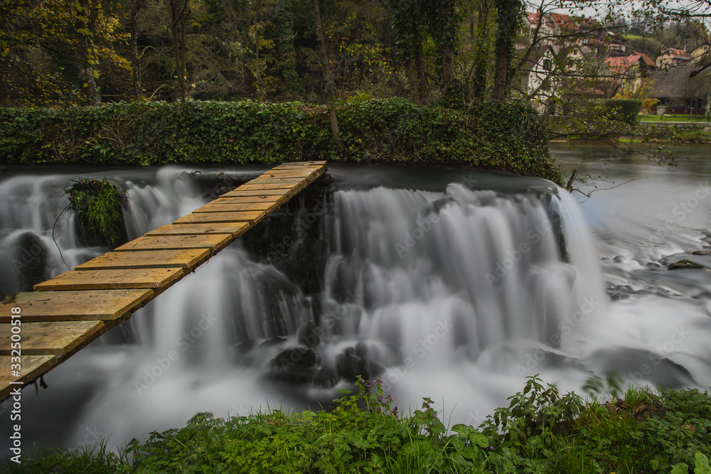 Naklejka premium Man made cascades on the river of Krka close to Zuzemberk in slovenia, used to power an old wood sawmill. Visible wooden bridge over the water.