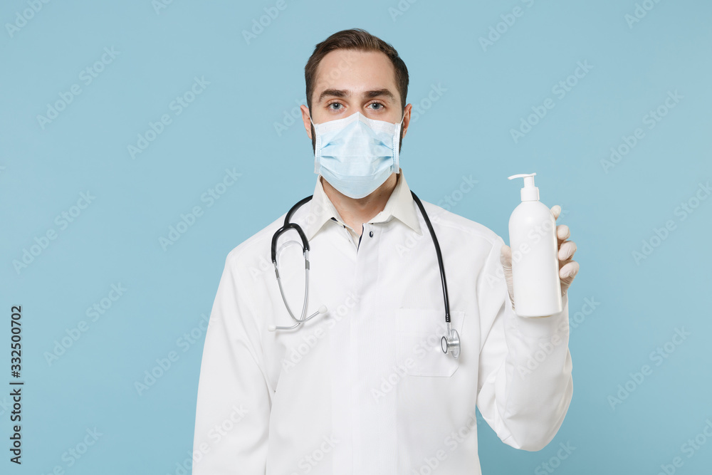 Male doctor man in medical gown sterile face mask gloves isolated on blue background. Epidemic pandemic spreading coronavirus 2019-ncov sars covid-19 flu virus. Hold bottle with antibacterial soap. Male doctor man in medical gown sterile face mask gloves isolated on blue background. Epidemic pandemic spreading coronavirus 2019-ncov sars covid-19 flu virus. Hold bottle with antibacterial soap.