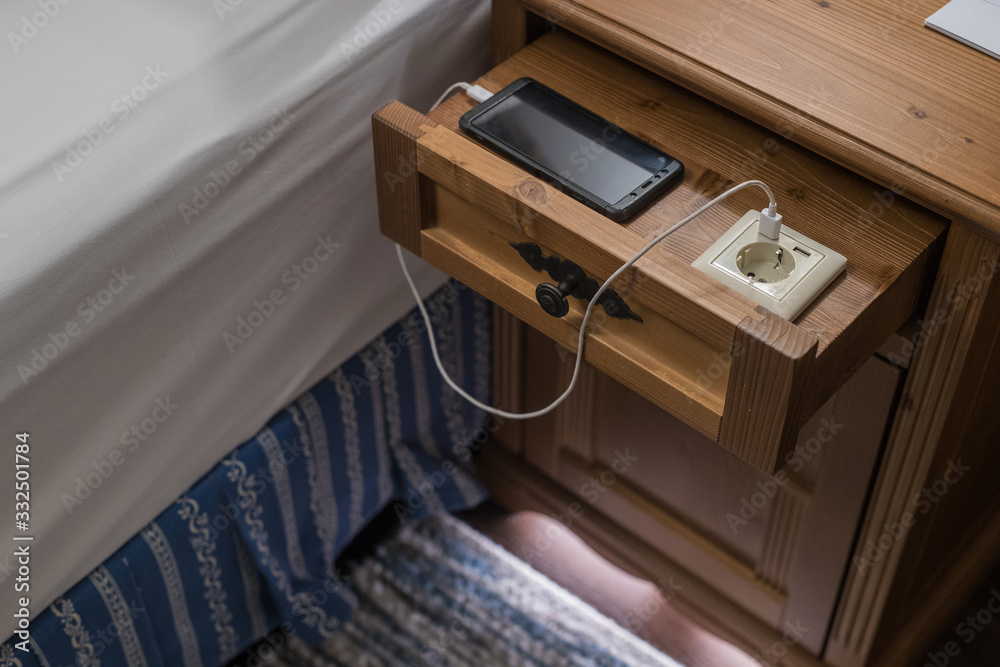 Fototapeta premium Electical socket with integrated USB charger in drawer of a modern hotel desk next to a bed. Smartphone charging next to a hotel bed.