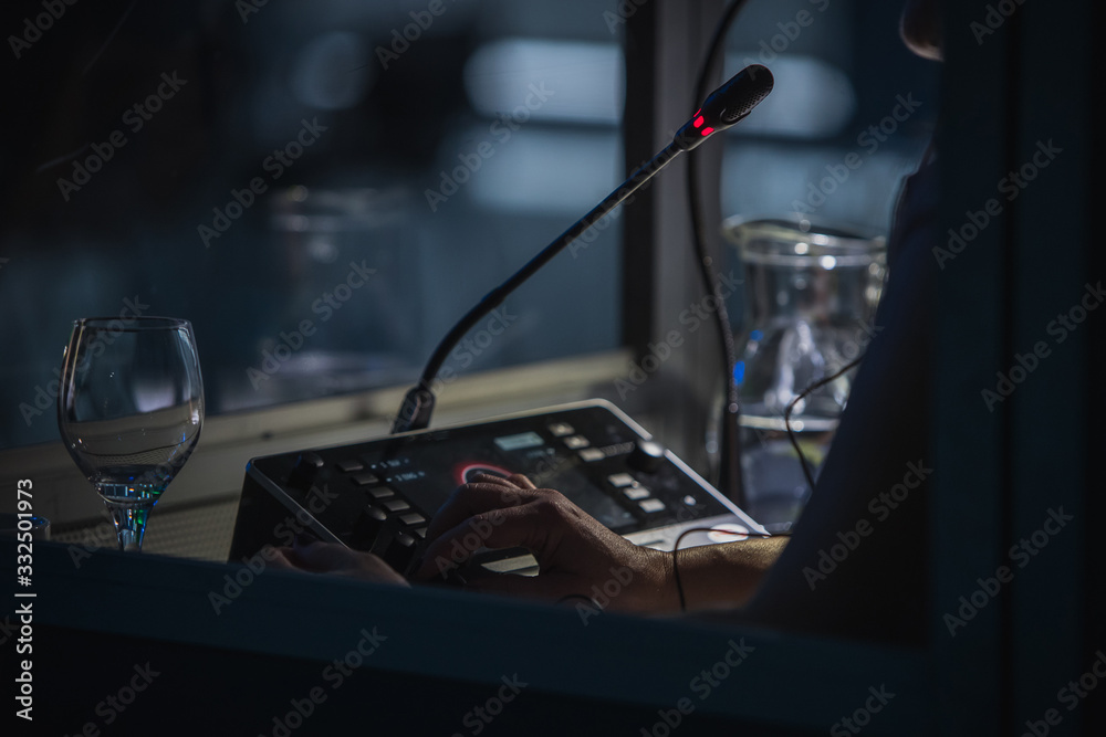 Translator or translation booth at a conference. Hand of a person for simultaneous translating is seen working in a booth. Glass of water next to a translator.