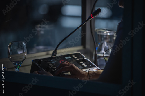 Translator or translation booth at a conference. Hand of a person for simultaneous translating is seen working in a booth. Glass of water next to a translator. photo