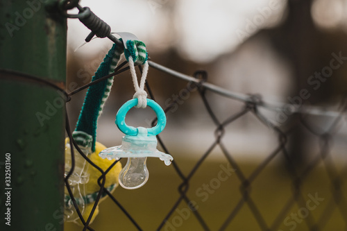 Lost child pacifier hanging on a metal fence waiting for the owner to come back. Dirty plastic kid pacifier lost outdoors.