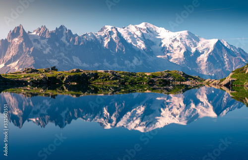 Range of white snowy peaks and hilly seaside reflecting in clear motionless lake in sunny day in Chamonix, Mont-Blanc