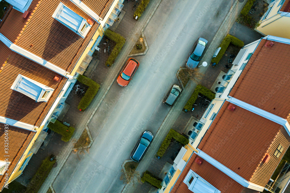 Obraz premium Aerial view of residential houses with red roofs and streets with parked cars in rural town area. Quiet suburbs of a modern european city.