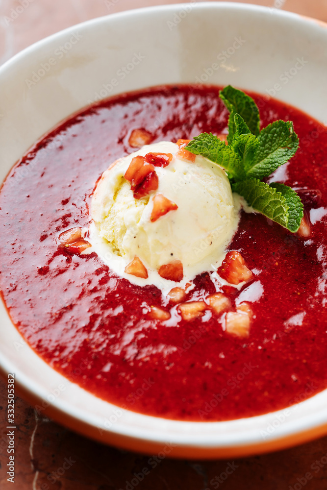 Top view of scoop of vanilla ice cream on plate with red syrup decorated with small pieces of strawberry and fresh green mint in restaurant Top view of scoop of vanilla ice cream on plate with red syrup decorated with small pieces of strawberry and fresh green mint in restaurant
