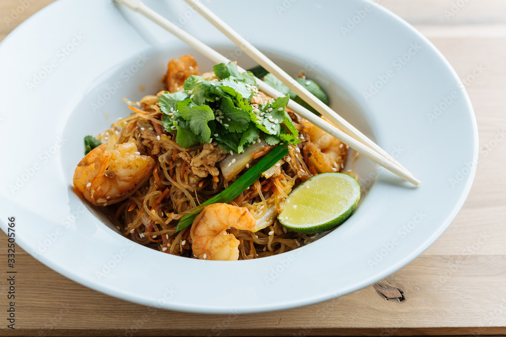 From above of tasty noodles with fried shrimps slices of lime and fresh parsley in plate with wooden chopsticks From above of tasty noodles with fried shrimps slices of lime and fresh parsley in plate with wooden chopsticks