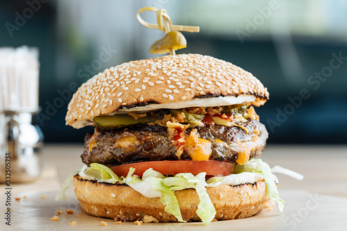 Closeup of juicy burger with tasty cutlet slices of tomatoes lettuce and cucumbers between soft roasted buns in restaurant