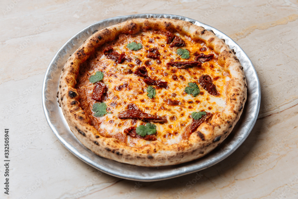 From above of juicy baked pizza served with cheese, herbs and dried tomato on table in restaurant From above of juicy baked pizza served with cheese, herbs and dried tomato on table in restaurant
