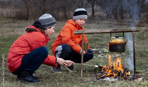two boys on a picnic in cold weather a warming bonfire with marshmallows and tea