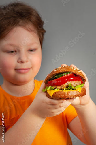 Child eats burger on grey background. Male child with hamburger