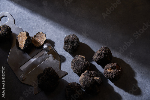 From above bunch of expensive black truffles placed near metal shaver on gray plaster surface photo