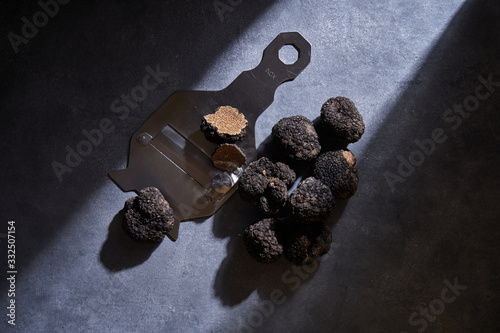 From above bunch of expensive black truffles placed near metal shaver on gray plaster surface