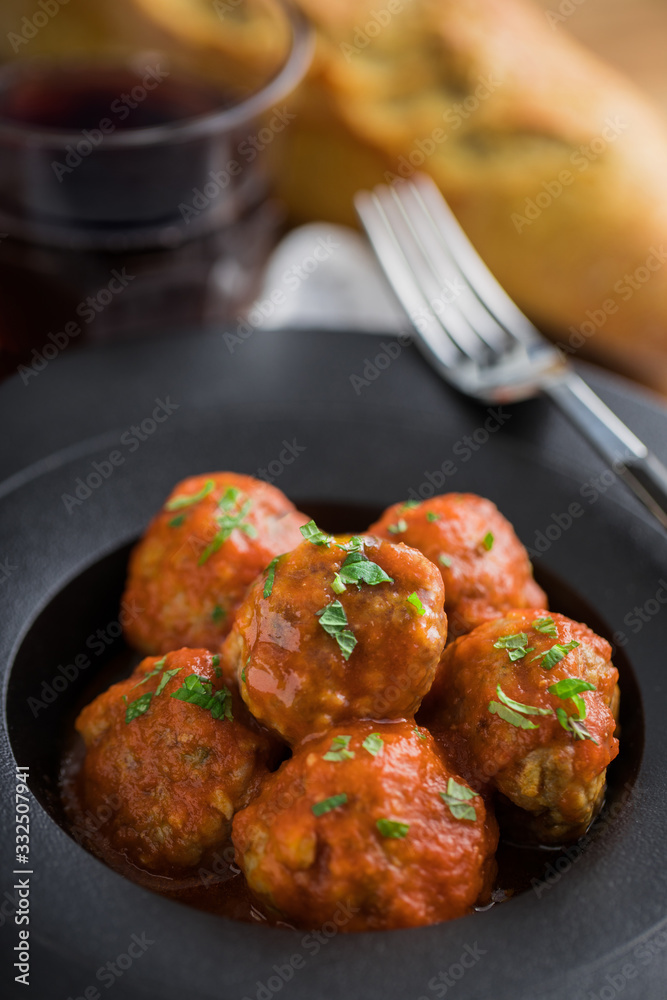 From above tasty cooked meatballs with tomato sauce serving with bread on black plate with cutlery and beverage on table