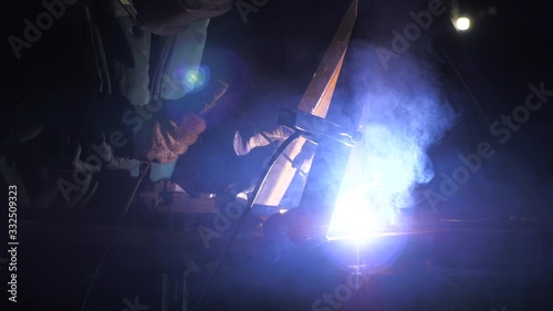 Industrial worker in a protective mask using modern welding machine for welding metal structures in industrial production at a metal processing plant. bright light and sparks from welding. © zoteva87