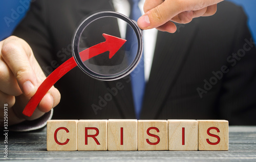 Businessman holds up arrow over blocks with the word Crisis. Increase instability of business and economy. Recession, stagnation, bankruptcy. Midlife crisis. Impoverishment. Debt and risk growth photo