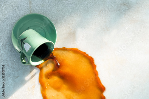 From above warm brown drink flowing from dropped green ceramic mug on saucer to gray table on cafe terrace