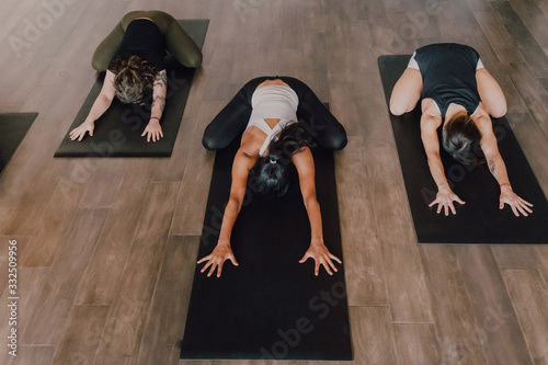 From above unrecognizable ladies in sportswear concentrating and lying in balasana position on sports mats on wooden floor in spacious workout room photo