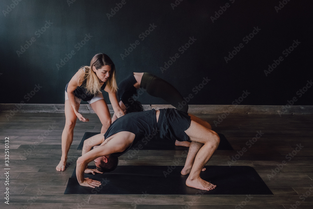 High angle of adult barefooted instructor in sportswear supporting man while teaching group of sporty people to do urdhva dhanurasana pose in contemporary workout room High angle of adult barefooted instructor in sportswear supporting man while teaching group of sporty people to do urdhva dhanurasana pose in contemporary workout room