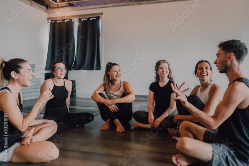 High angle of young diverse women and men in sportswear sitting in lotus pose and having interest discussions while resting after group training in contemporary yoga studio photo