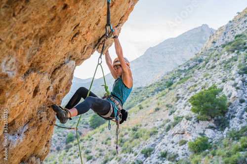 From below side view of active focused youthful female alpinist climbing on cliff in summer day photo