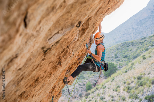 From below side view of active focused youthful female alpinist climbing on cliff in summer day photo