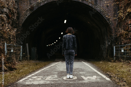 Back view of stylish woman in black leather jacket looking at dark tunnel with illumination inside on marked with inscription slow road in United Kingdom photo