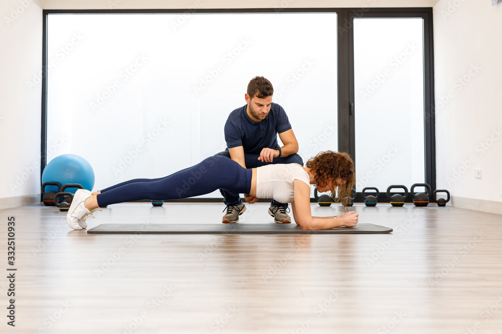 Side view of strong woman in plank position with male personal trainer in modern gym Side view of strong woman in plank position with male personal trainer in modern gym