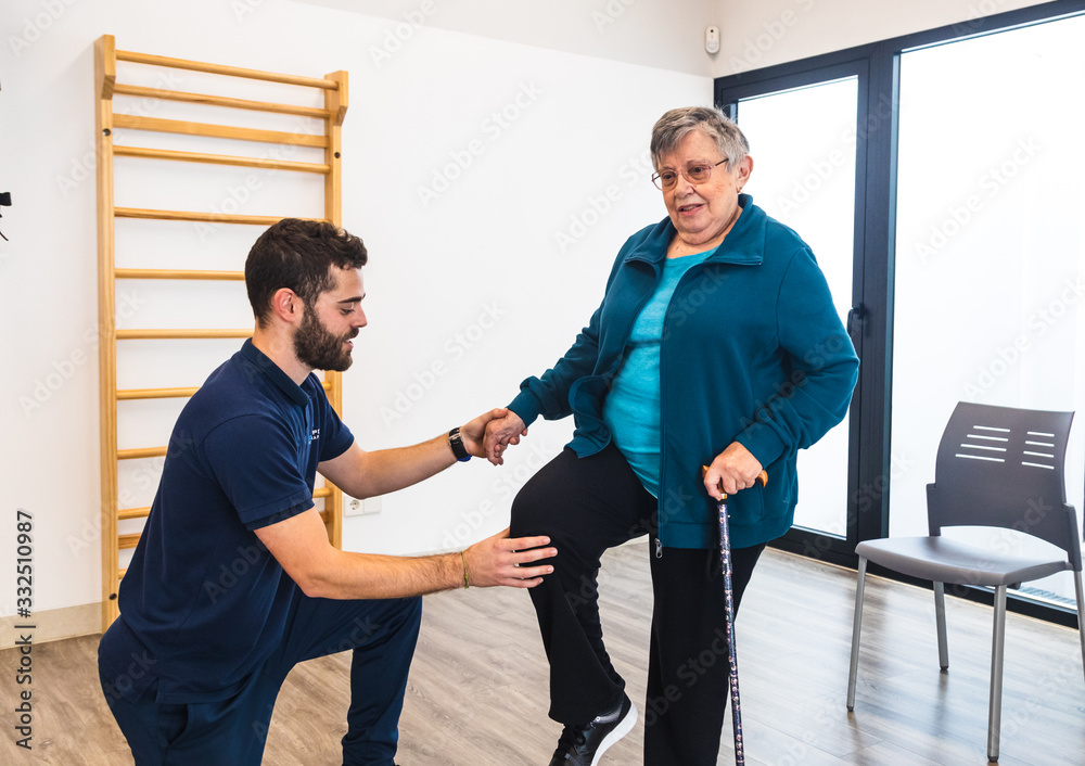 Male instructor supporting old woman using train in gym Male instructor supporting old woman using train in gym