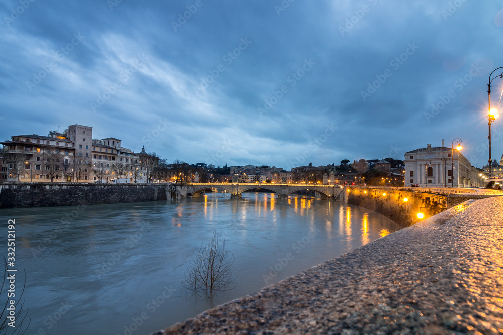 Long exposure view of the Tiber river with bridge in the background on a rainy autumn sunset with light set and reflection, Rome, Italy. Top view.