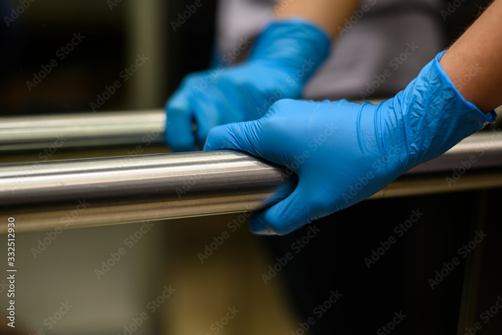 A female hand in a protective blue glove holds on to the handrail. Antibacterial protection. Quarantine. The concept of self-isolation during a pandemic and epidemic.