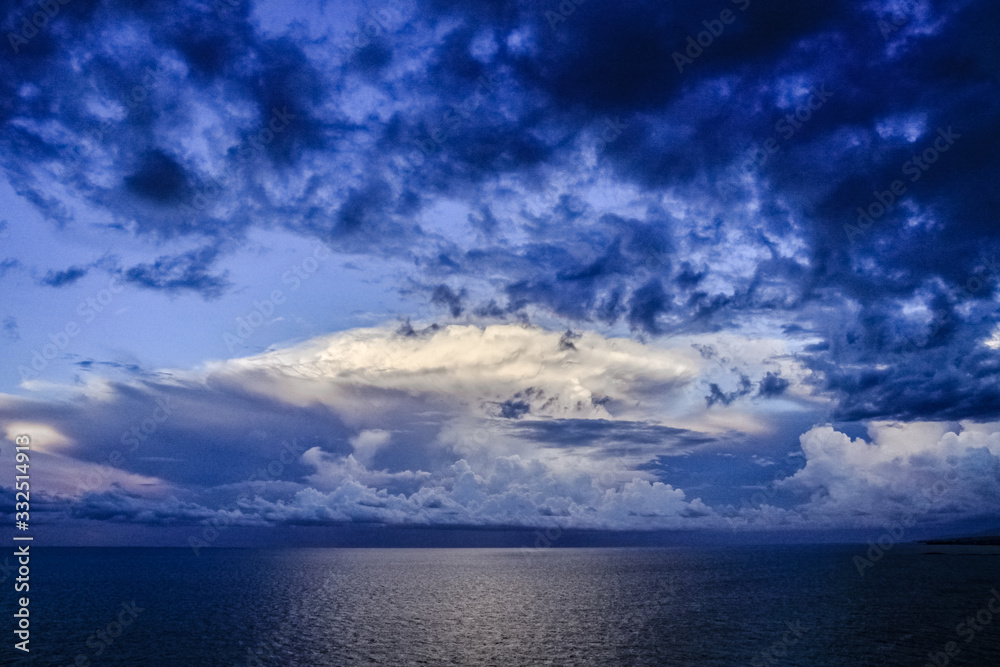 Panoramic view of ocean waters horizon line with dramatic cumulus thunderstorm cloudscape in blue sky background.