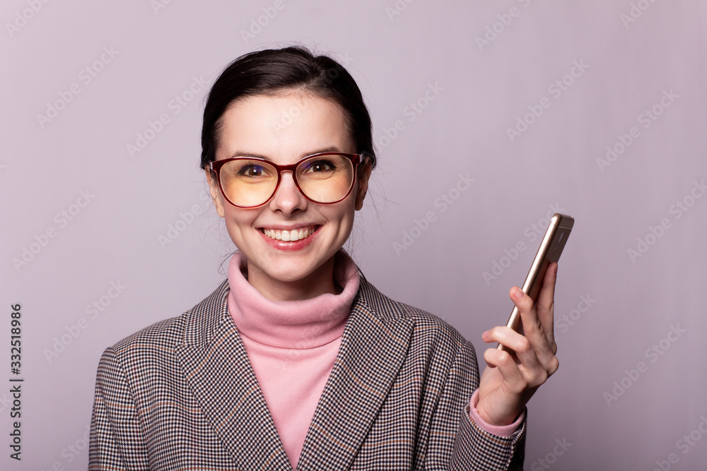 beautiful girl in a pink turtleneck, gray jacket, glasses for sight communicates on the phone on a gray background beautiful girl in a pink turtleneck, gray jacket, glasses for sight communicates on the phone on a gray background