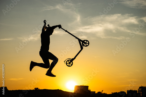 silhouette of a man riding and jumping on kick scooter with beautiful sunrise on background