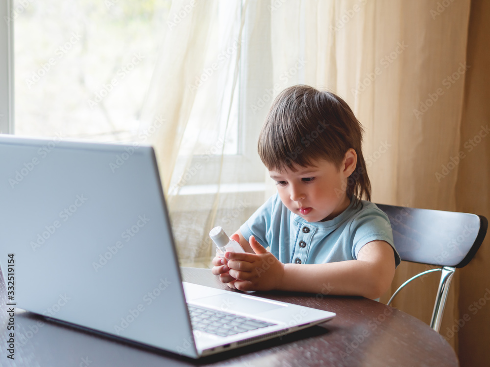 Self-isolation because of coronavirus outbreak. Child is holding bottle of medical sanitizer gel for skin sterilization. Laptop on table. Self-isolation because of coronavirus outbreak. Child is holding bottle of medical sanitizer gel for skin sterilization. Laptop on table.