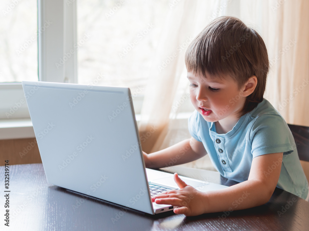 Curious toddler boy explores the laptop and presses buttons on computer keyboard.