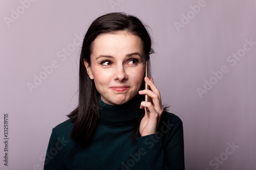 girl in a green turtleneck talking on the phone, portrait on a gray background