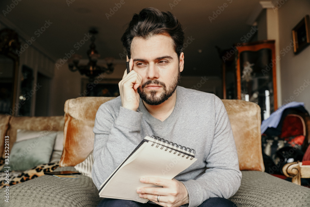 Fototapeta premium Młody brodaty hipster próbuje białego czegoś w zeszycie.