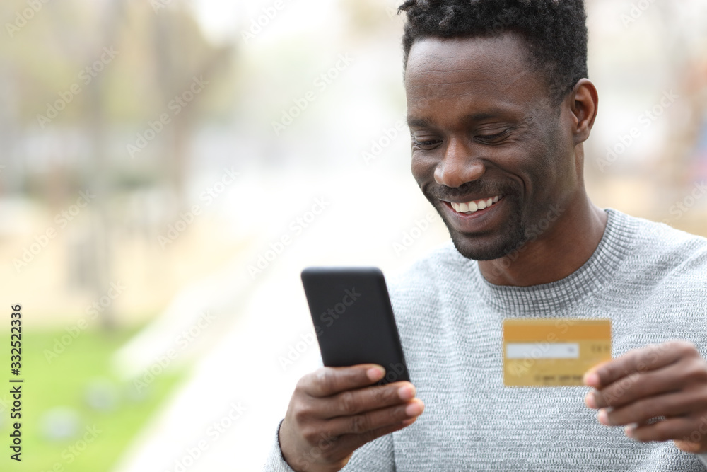 Happy black man paying online with credit card on phone