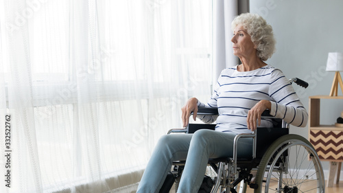 Pensive sick disabled old lady sit in wheelchair look in distance feel lonely at home or retirement house, thoughtful sad handicapped mature woman in wheel chair thinking, elderly disability concept