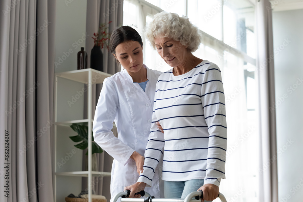 Young female nurse help old lady patient with walking frame in home or hospital, woman doctor or caregiver assist senior elderly grandmother with walker, physiotherapy, rehabilitation concept Young female nurse help old lady patient with walking frame in home or hospital, woman doctor or caregiver assist senior elderly grandmother with walker, physiotherapy, rehabilitation concept