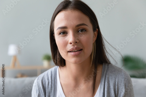 Close up headshot portrait of beautiful millennial girl sit on couch look at camera having video call at home, pretty young woman talk chat online using wireless connection, Internet dating service