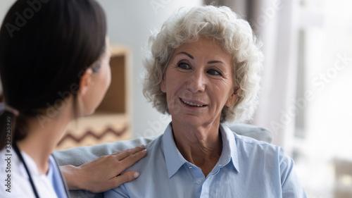 Attentive female caregiver visit positive senior old lady talking to retired lonely woman at home, caring doctor give help support consult mature grandmother, elderly healthcare concept