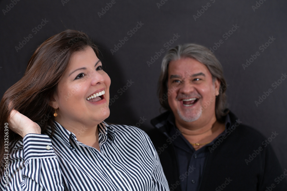 Couple Studio portrait. She is in the foreground and he is in the background. She is laughing happy looking away and he looks at her also laughing. Couple Studio portrait. She is in the foreground and he is in the background. She is laughing happy looking away and he looks at her also laughing.
