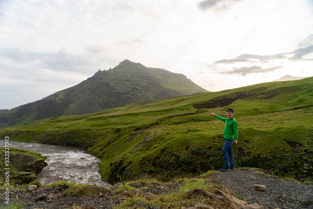 Young hiker man with river and green mountains on background on the Fimmvorduhals hiking trail in Iceland. Concept of freedom movement and freedom